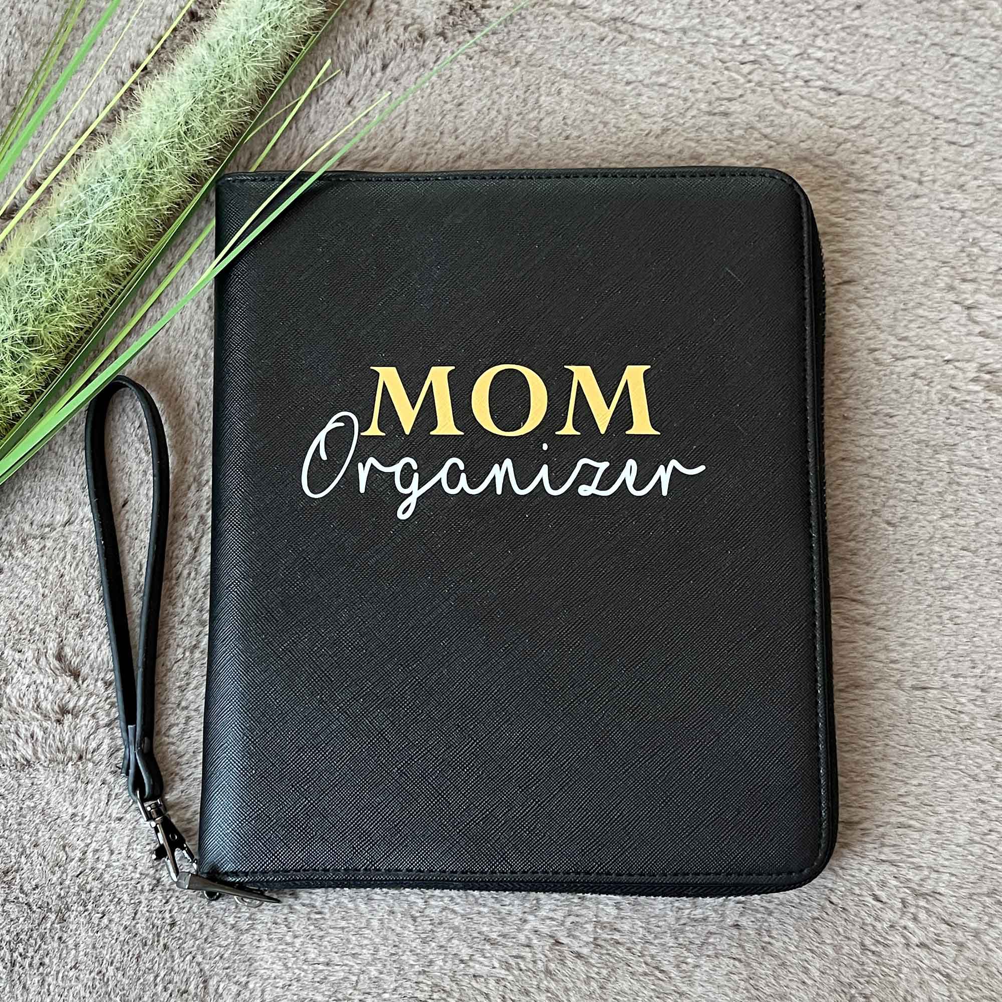 Schwarzer MOM Organizer auf flauschiger Decke – stilvolle Mutterpasshülle für Schwangerschaft und Babyzeit.