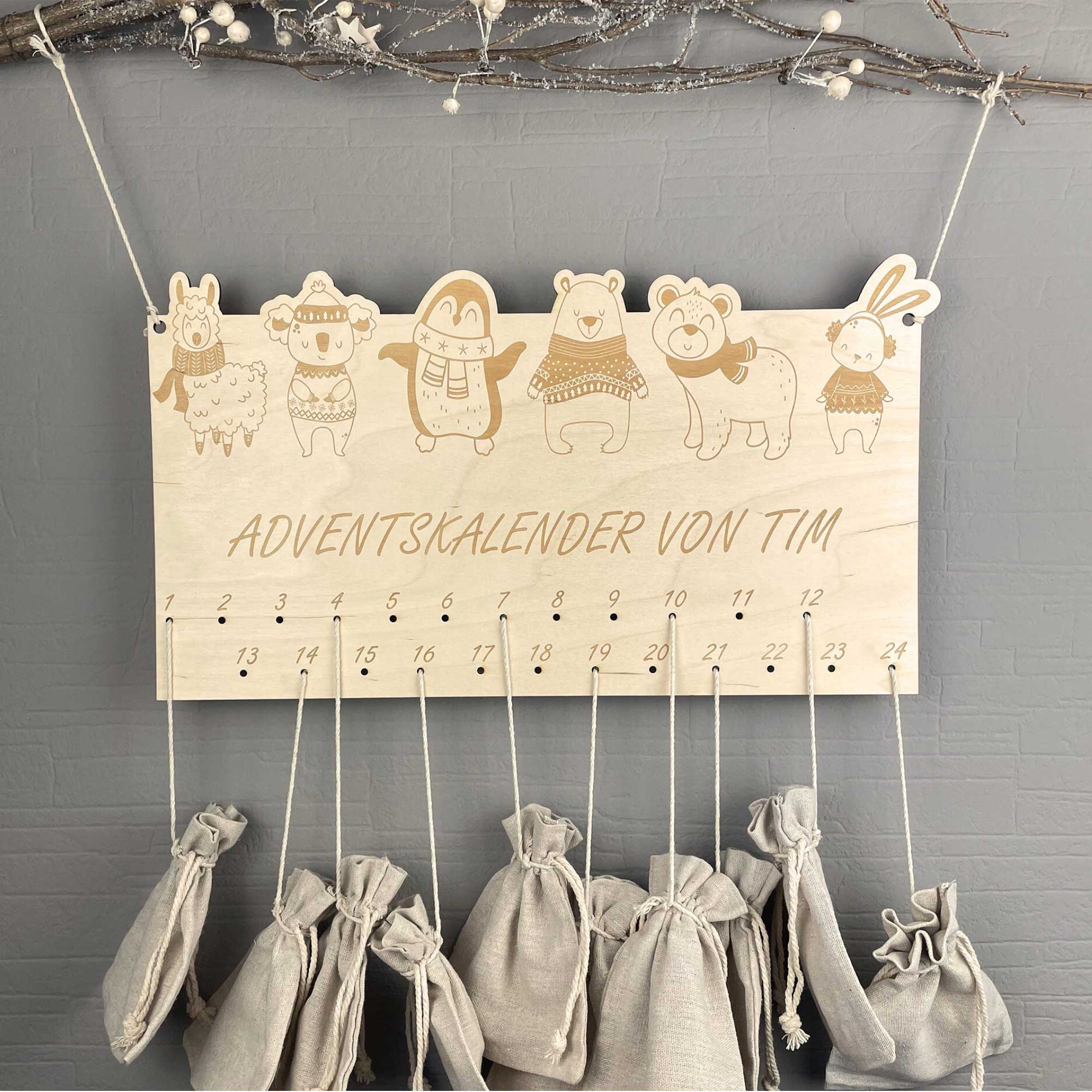 DIY Adventskalender aus Holz mit Wintertieren und Namen, aufgehängt an einem Ast mit Jutesäckchen – Adventskalender zum Selbstbefüllen