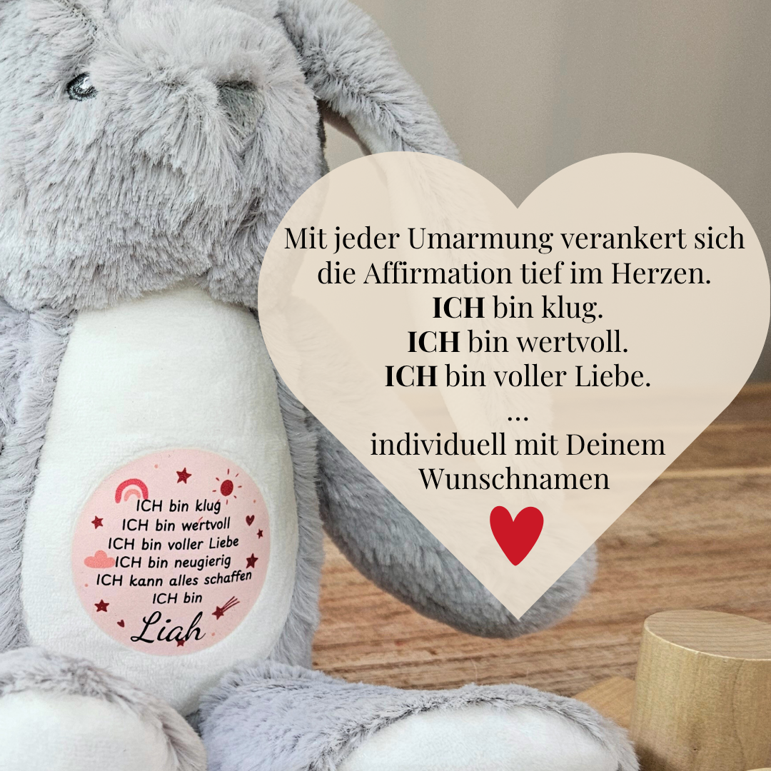 Herzförmiger Spruch: „Mit jeder Umarmung verankert sich die Affirmation“ – auf Hase mit rosa Aufdruck und Name.
