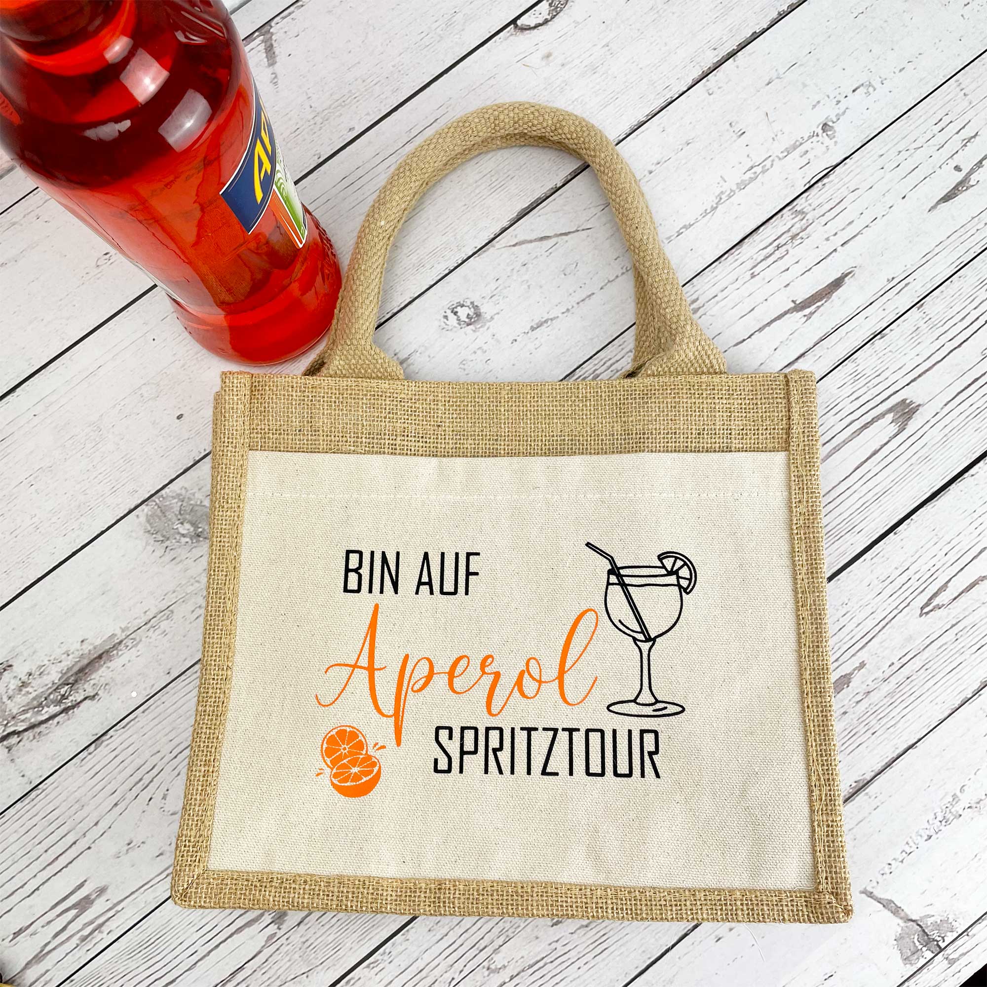 Jutetasche mit Aperol Spritz Motiv und Flasche – dekorativ auf einem Holztisch platziert