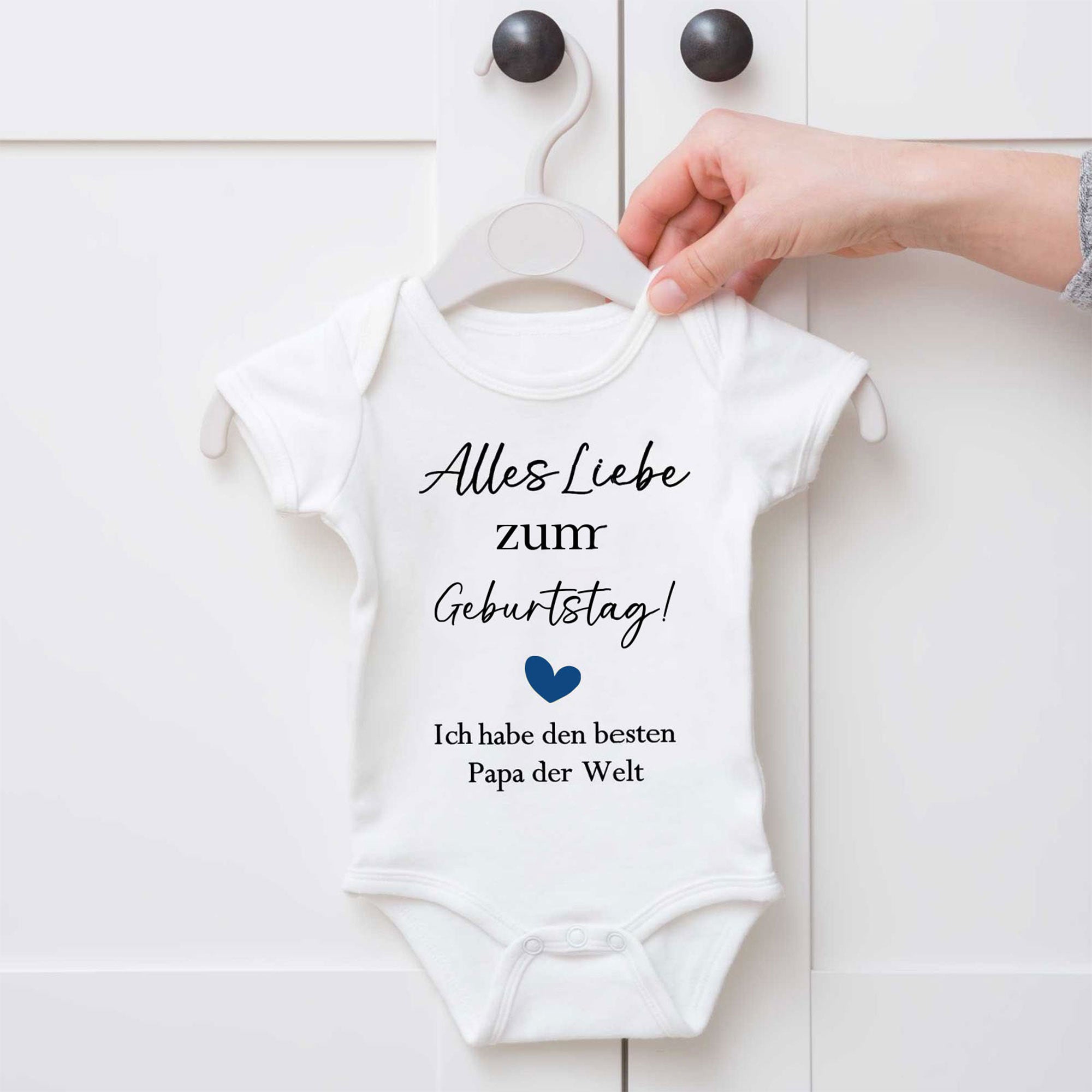 Weißer Baby Body zum Geburtstag für Papa mit Herzmotiv – aufgehängt am Schrank