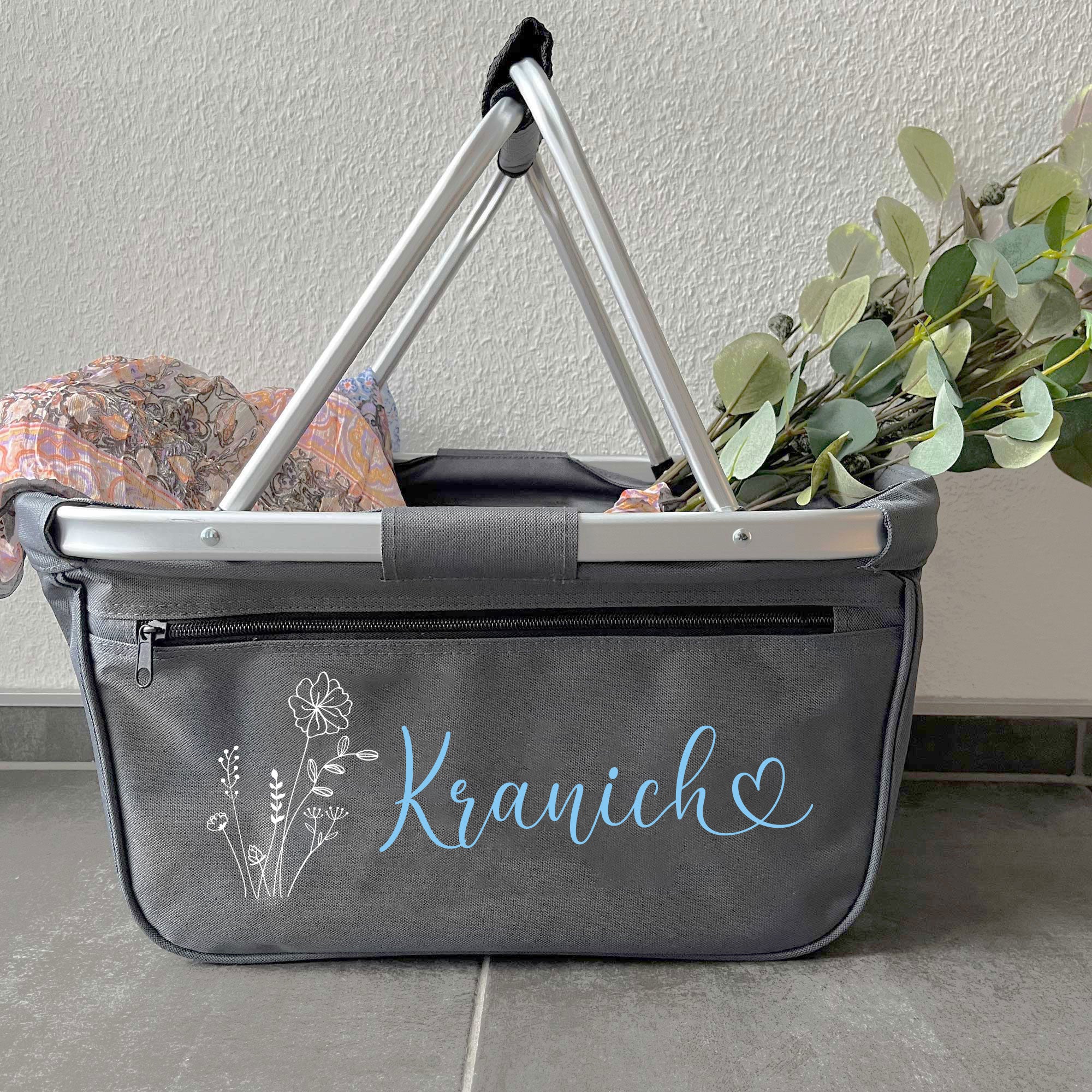 Personalisierter Einkaufskorb mit Name Kranich und Herzsymbol vor heller Wand mit Eukalyptus
