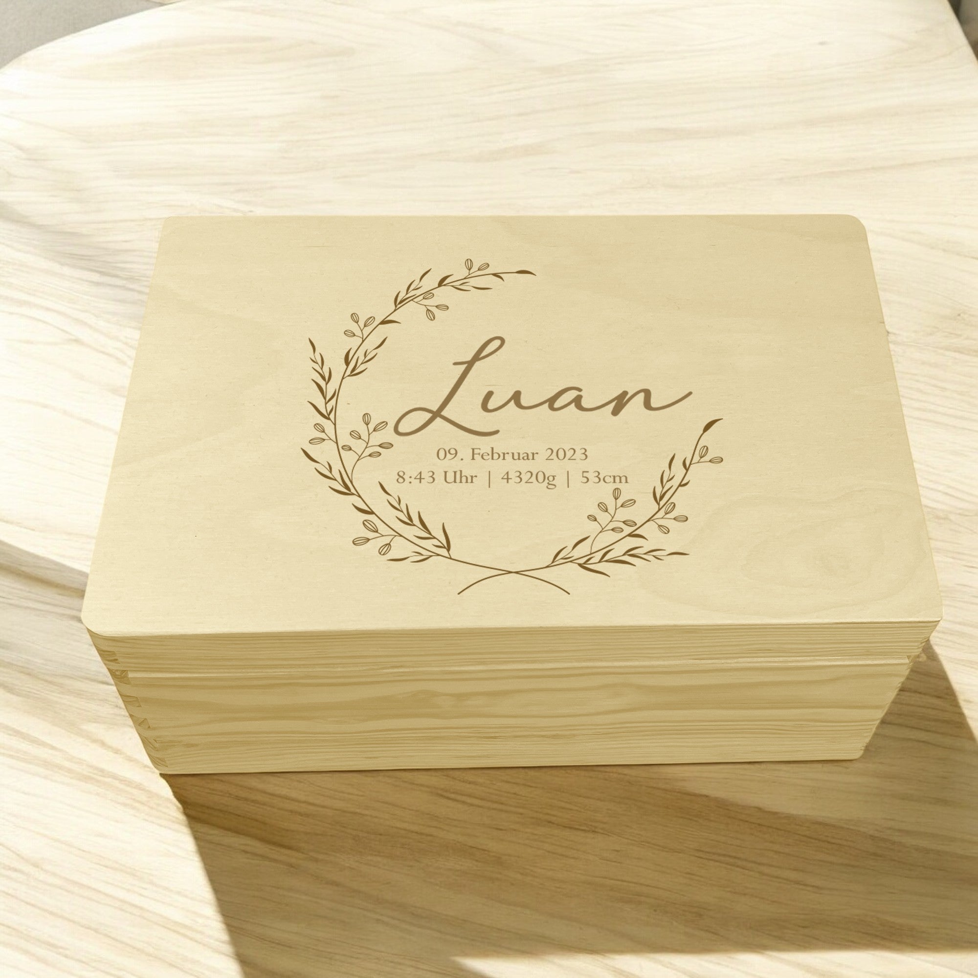 Personalisierte Holzkiste mit Blumenkranz und Gravur von Name und Geburtsdaten auf Arbeitsplatte