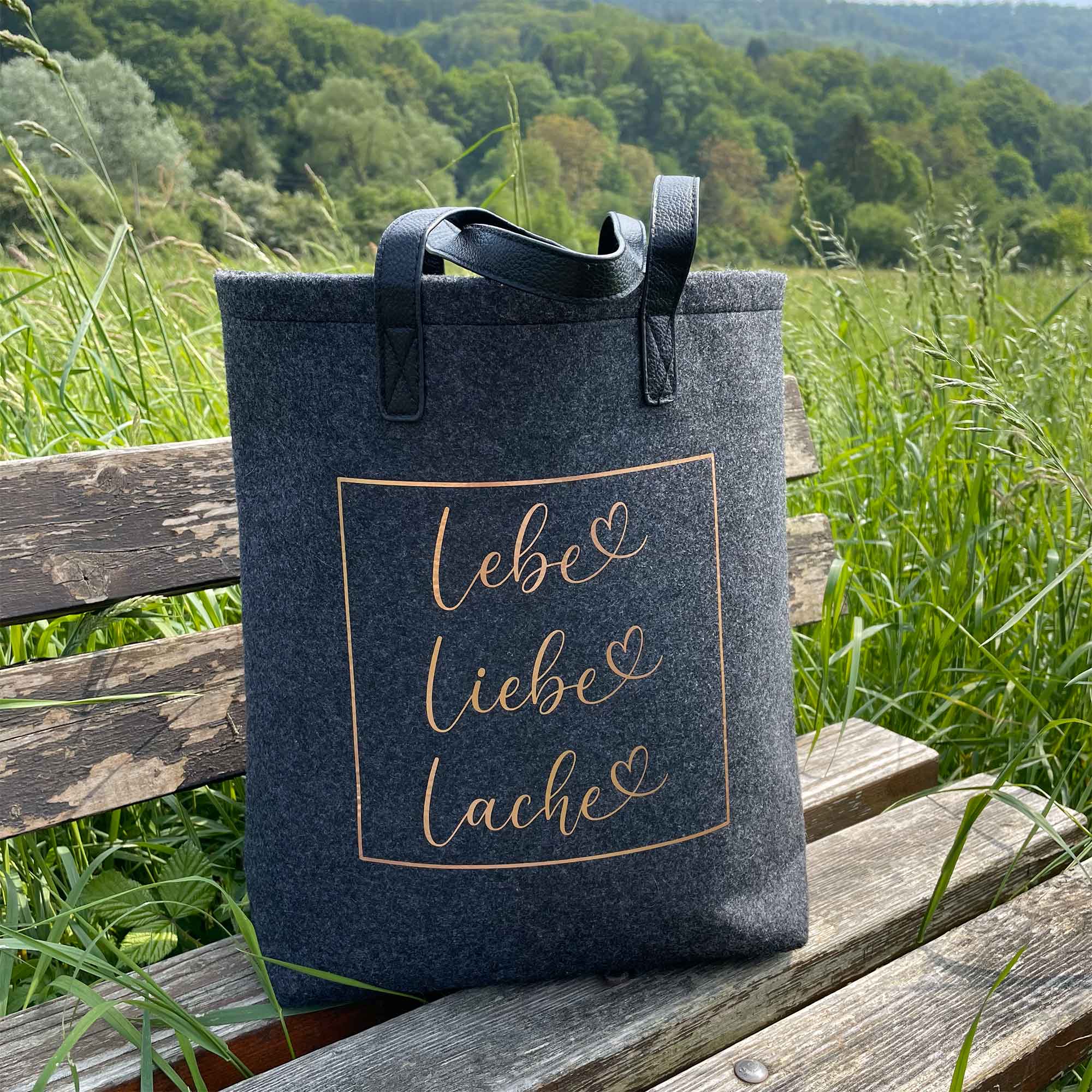 Filztasche mit Lebe Liebe Lache Spruch auf Parkbank im Grünen – perfektes Lebe Liebe Lache Geschenk