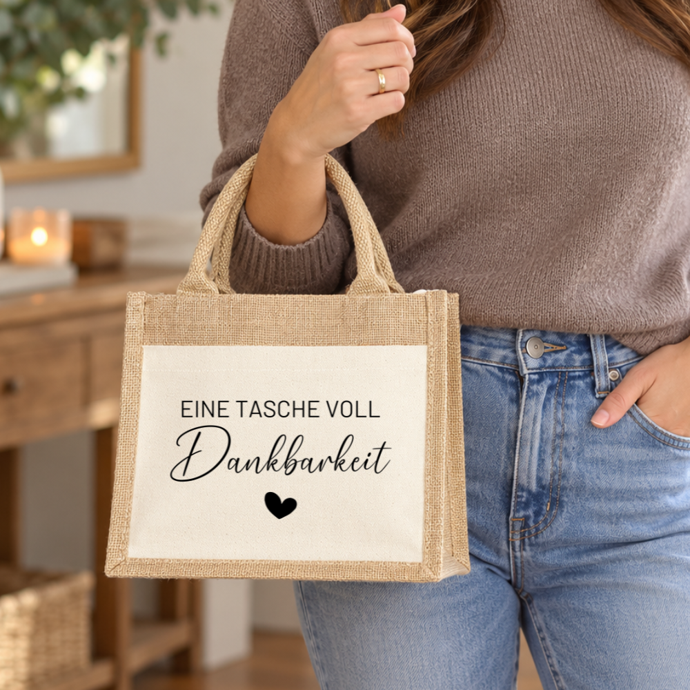 Frau mit kleiner naturfarbener Jutetasche und schwarzem Dankbarkeit-Aufdruck, zeigt die handliche Größe der Geschenktasche im Alltag.