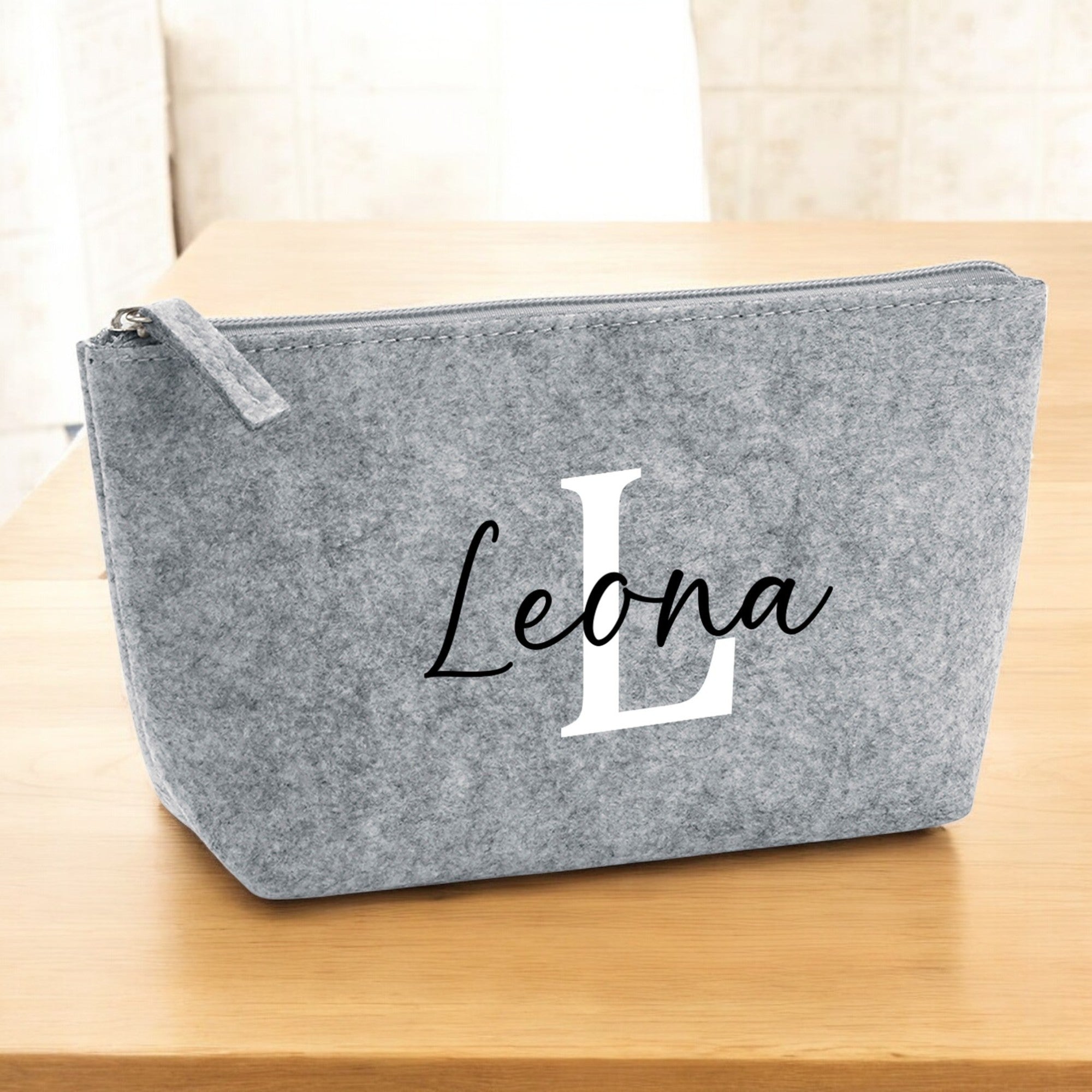 Kleine Kosmetiktasche aus grauem Filz mit personalisiertem Namen auf Holztisch