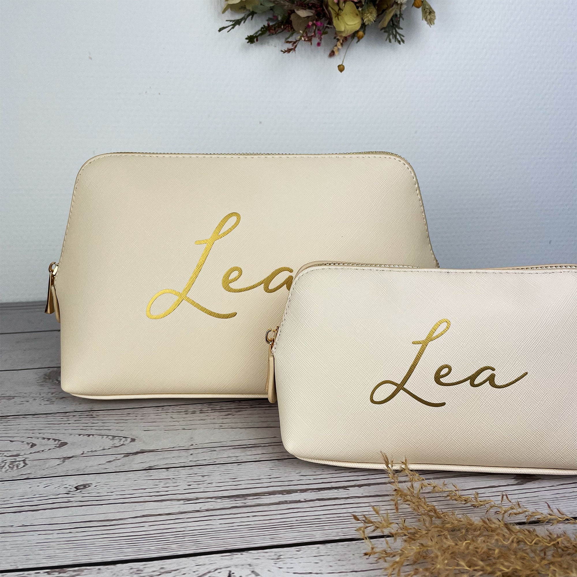 Zwei cremefarbene Kosmetiktaschen mit personalisiertem Namen Lea auf Holzuntergrund