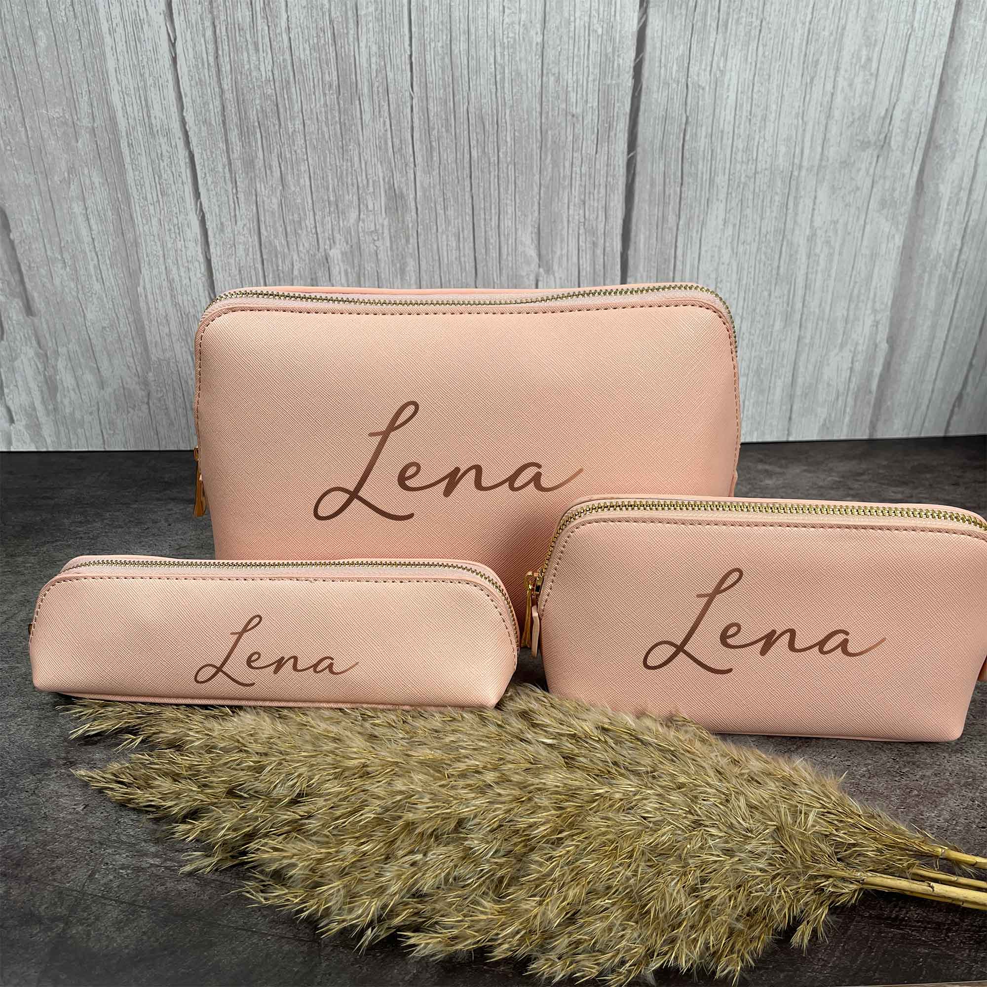 Drei rosa Kosmetiktaschen mit personalisiertem Namen Lena vor Holzoptik-Hintergrund