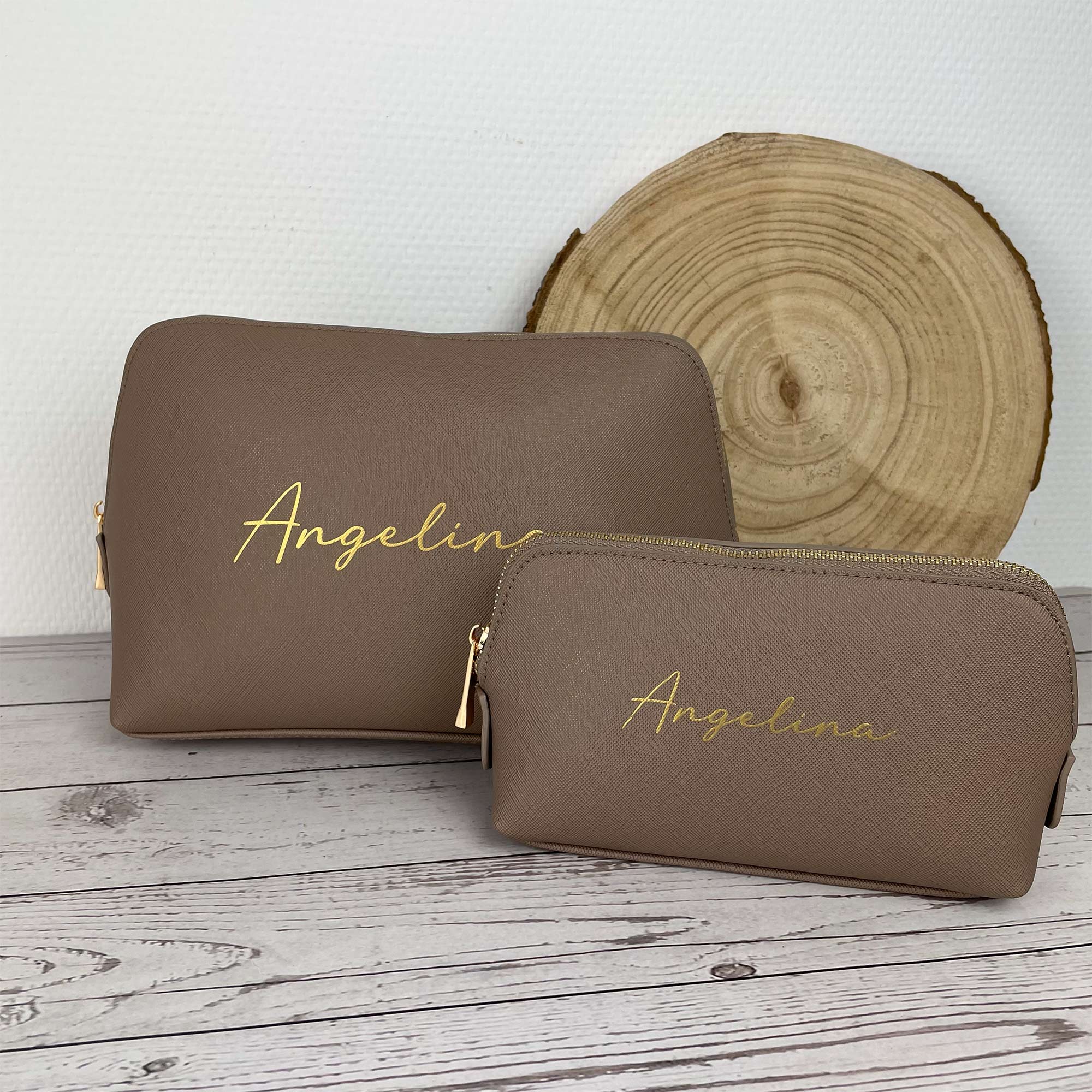 Zwei Kosmetiktaschen in Taupe mit goldenem Namen Angelina vor Holzscheibe