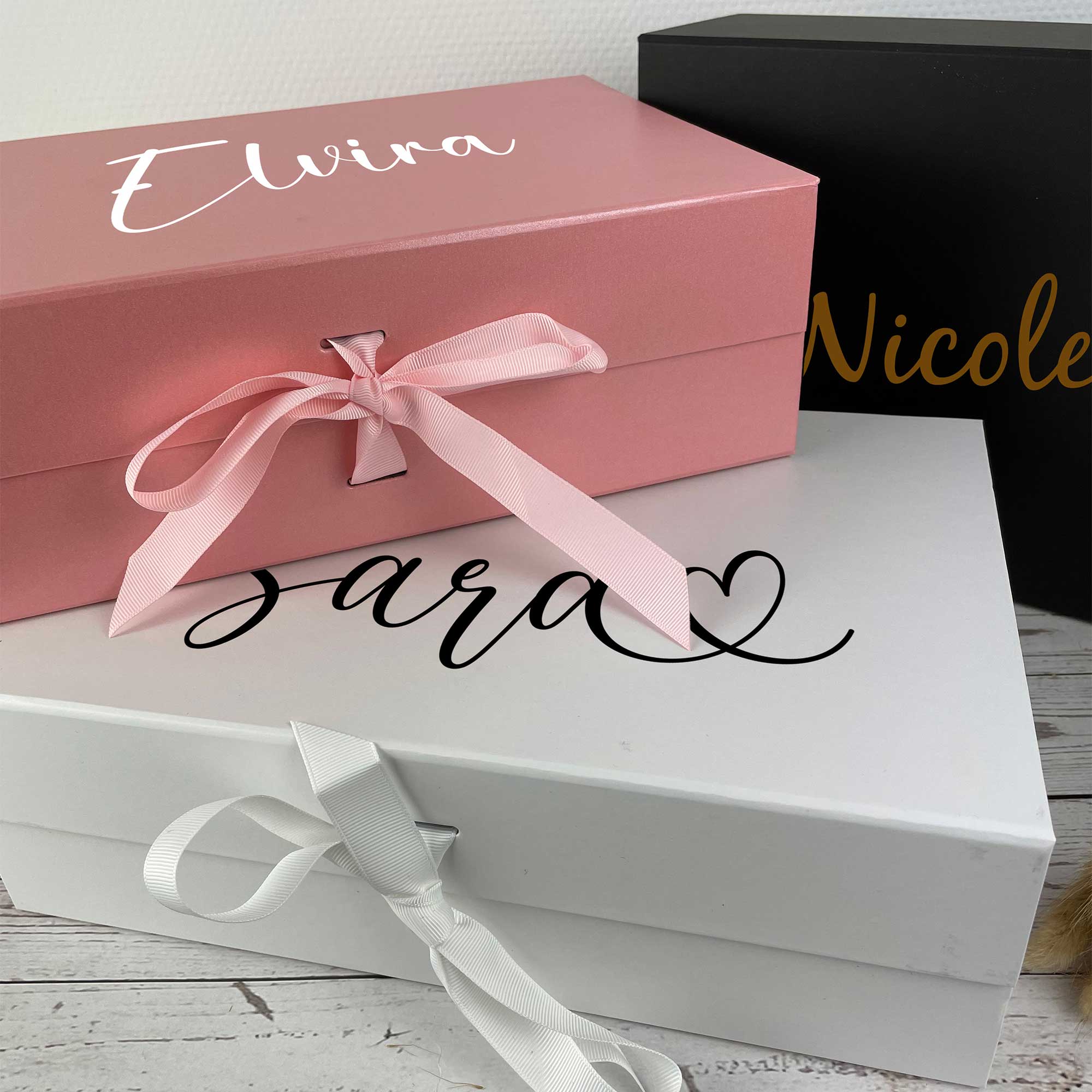Drei Geschenkboxen in Rosa, Weiß und Schwarz mit Namen