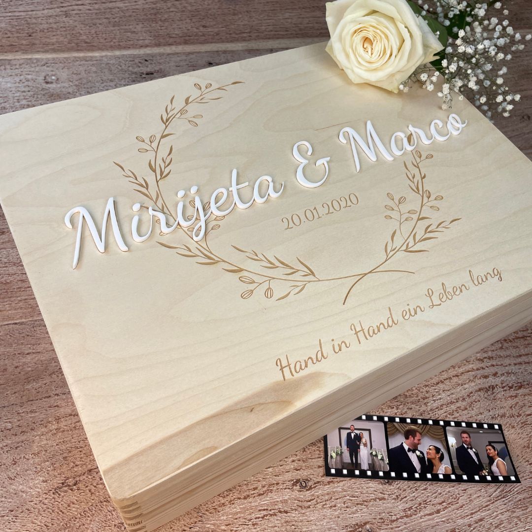 Detailaufnahme einer personalisierten Hochzeitskiste mit 3D-Namen und Gravur, dekoriert mit weißer Rose und Hochzeitsfotos.