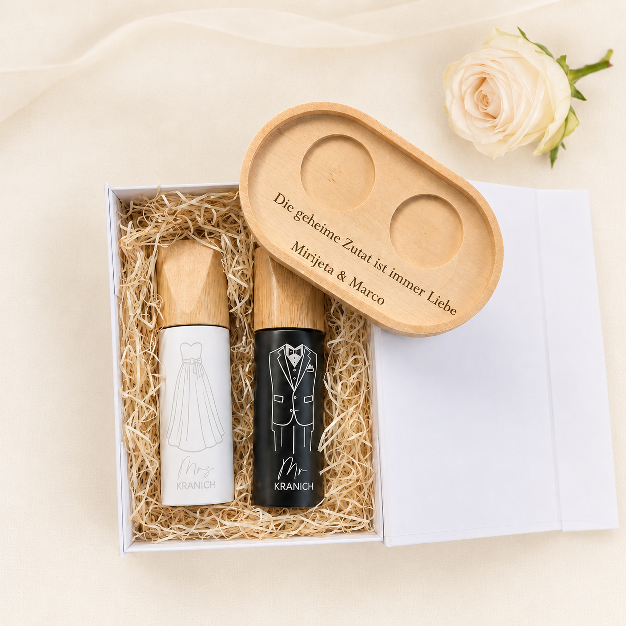 Geöffnete Geschenkbox mit personalisierten Salz- und Pfeffermühlen, graviertem Holztablett und dekorativer Holzwolle.