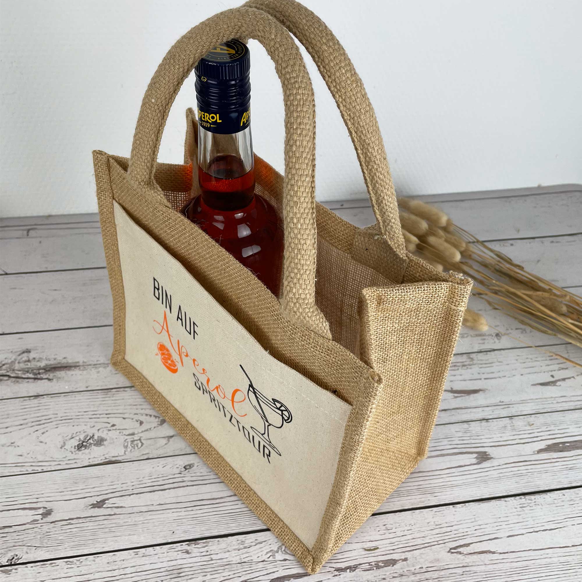 Jutetasche 'Bin auf Aperol Spritztour' mit Flasche – seitlich fotografiert auf Holztisch