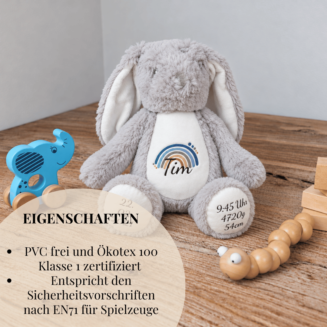 Personalisierter Kuschelhase in Grau mit Regenbogendesign und individuell aufgedruckten Geburtsdaten des Kindes.